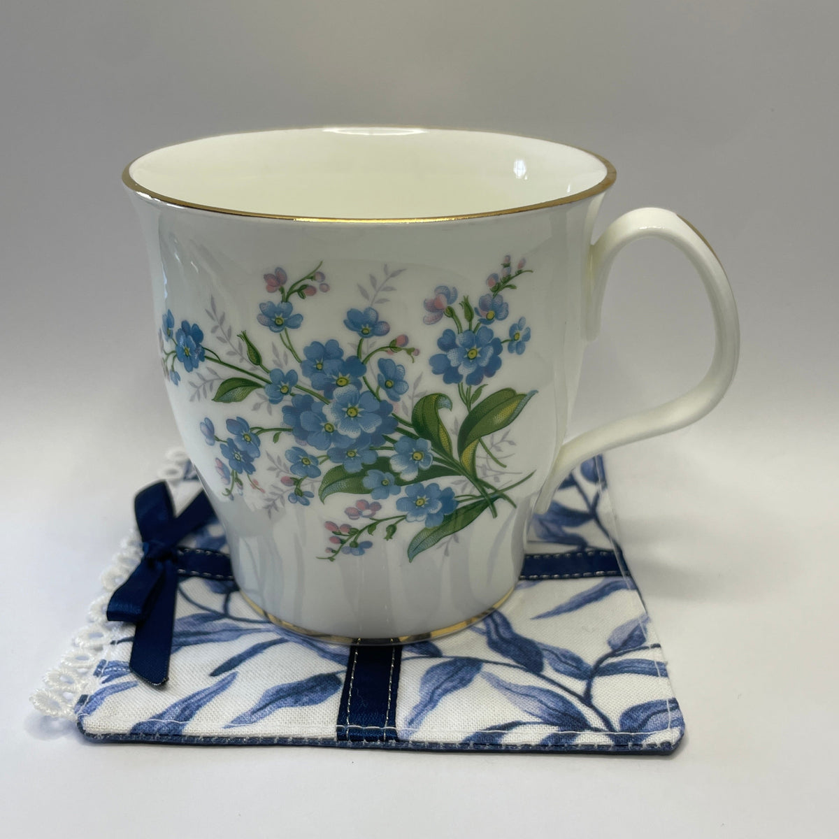 a cup of tea in a forget me not mug on a blue willow fabric coaster